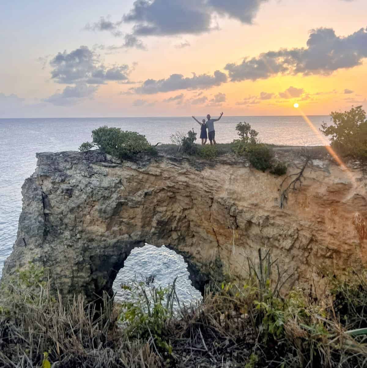 Couple standing on a rocky arch outcrop in Anguilla with the sun setting into the Ocean