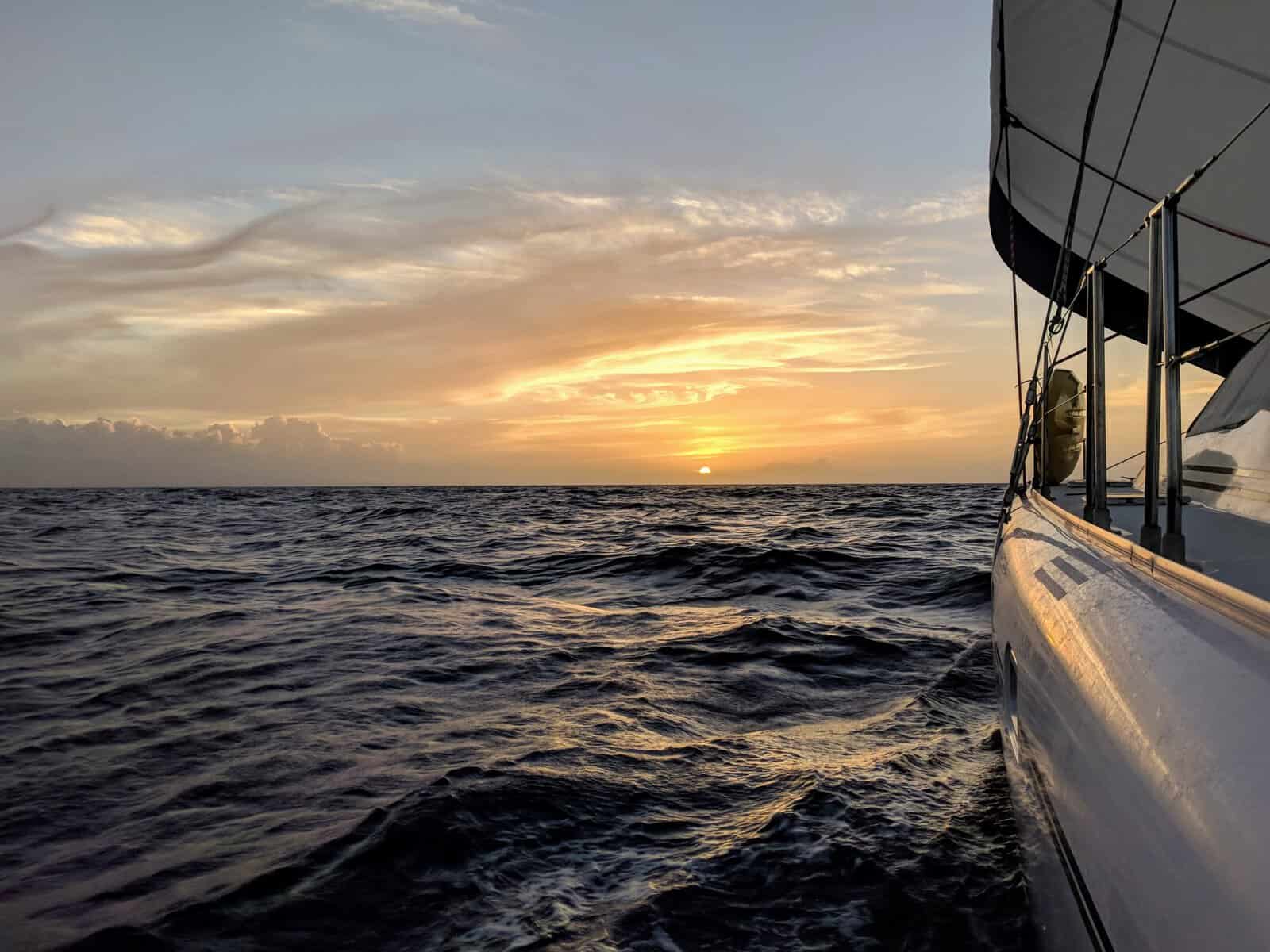 sunset into the ocean reflecting off the side of a charter sailboat