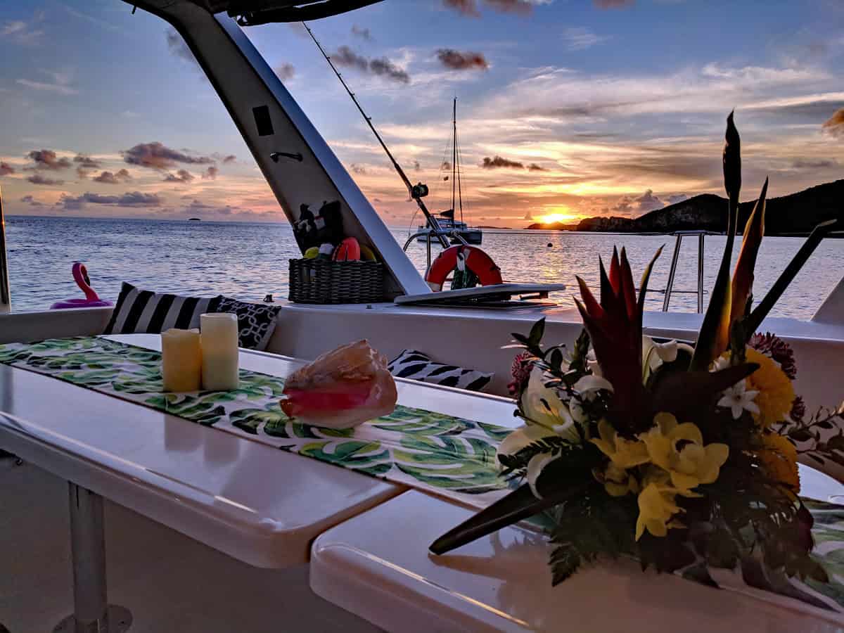 Sunset from a charter sailboat cockpit with floral table runner, candles, conchshell and fresh flowers