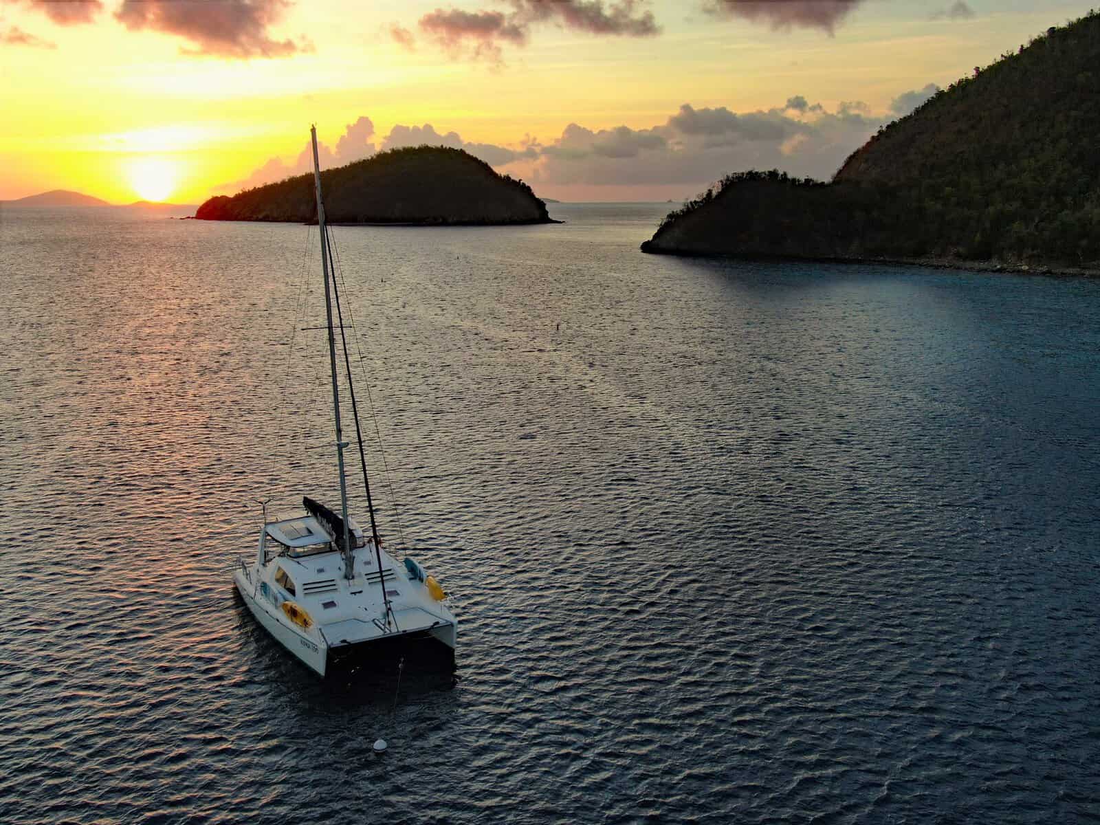 charter sailboat alone in a bay in the Caribbean with the sun setting in the background