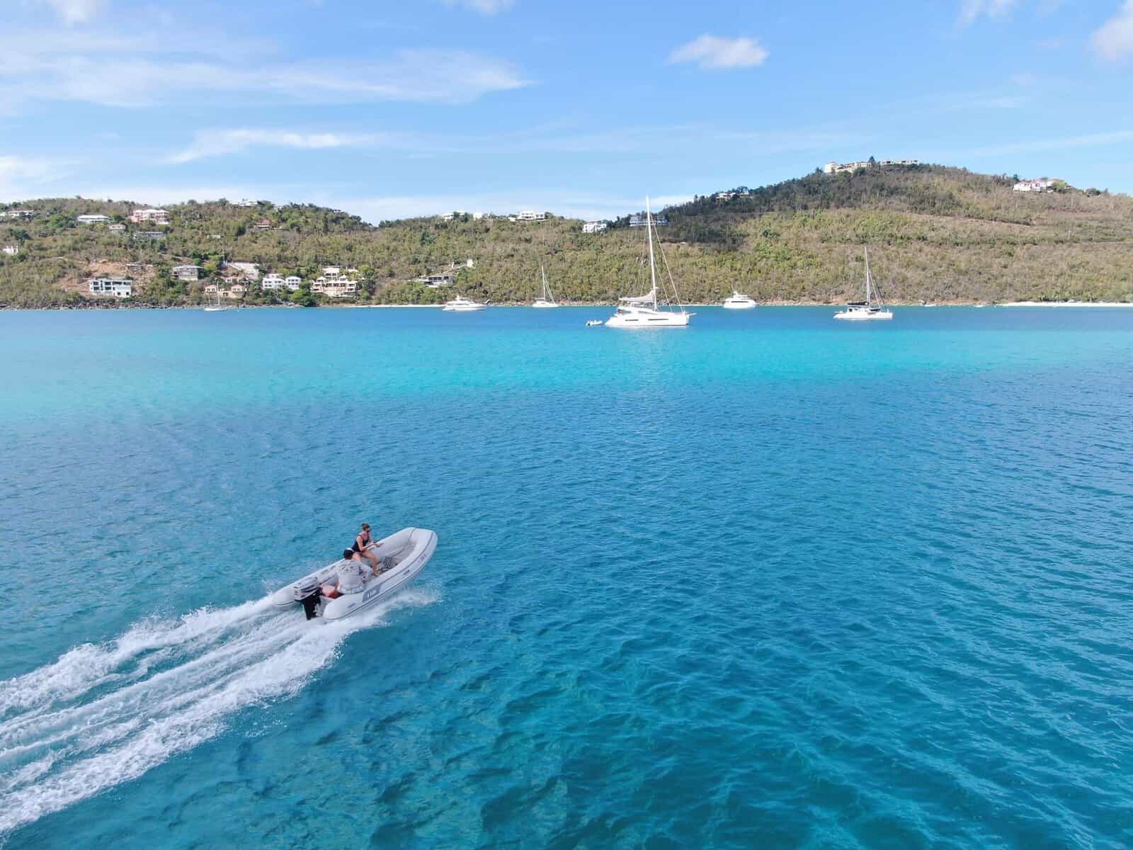 dinghy moving through bright teal water in the Caribbean with charter sailboats in the background