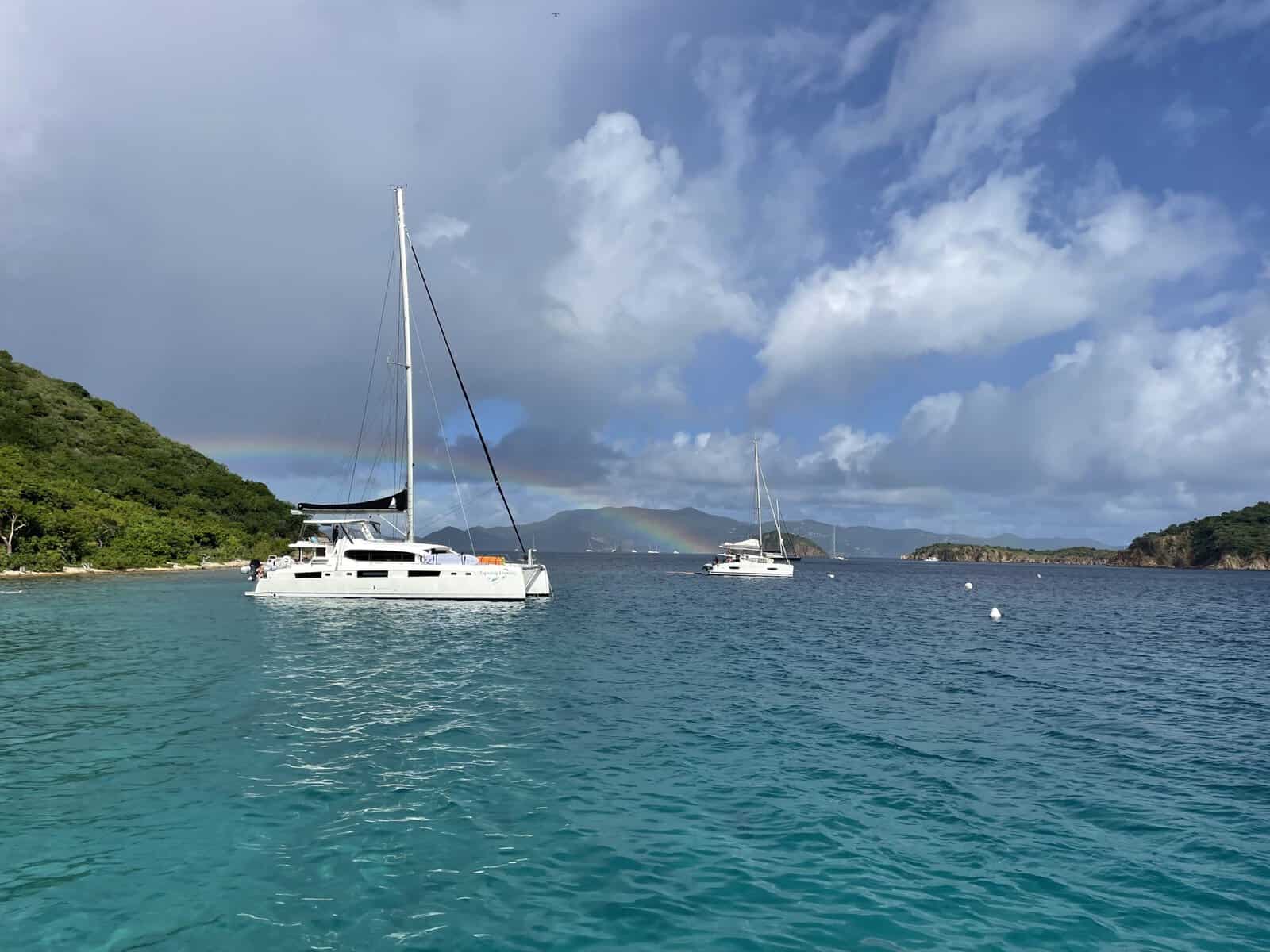 charter sailboat catamaran in the Caribbean with a rainbow and green island hills in the background