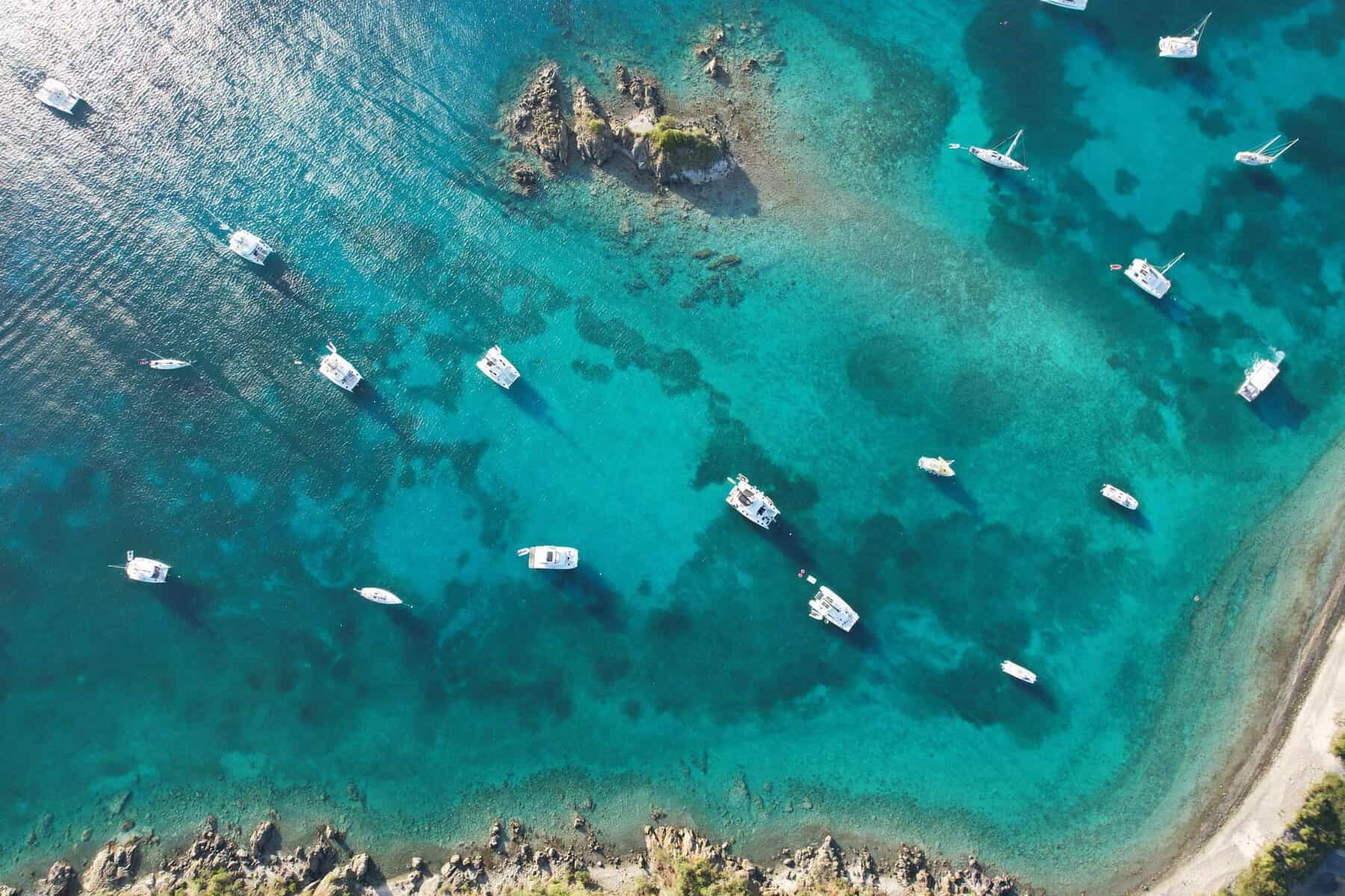 aerial view of 18 charter sailboats in a bay with bright turquoise blue water in the Caribbean