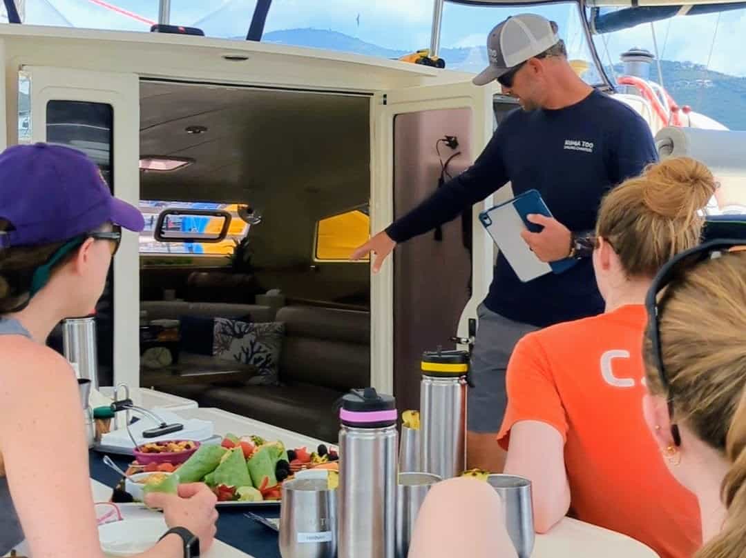 male captain giving safety briefing on a charter sailboat with back of guests in foreground