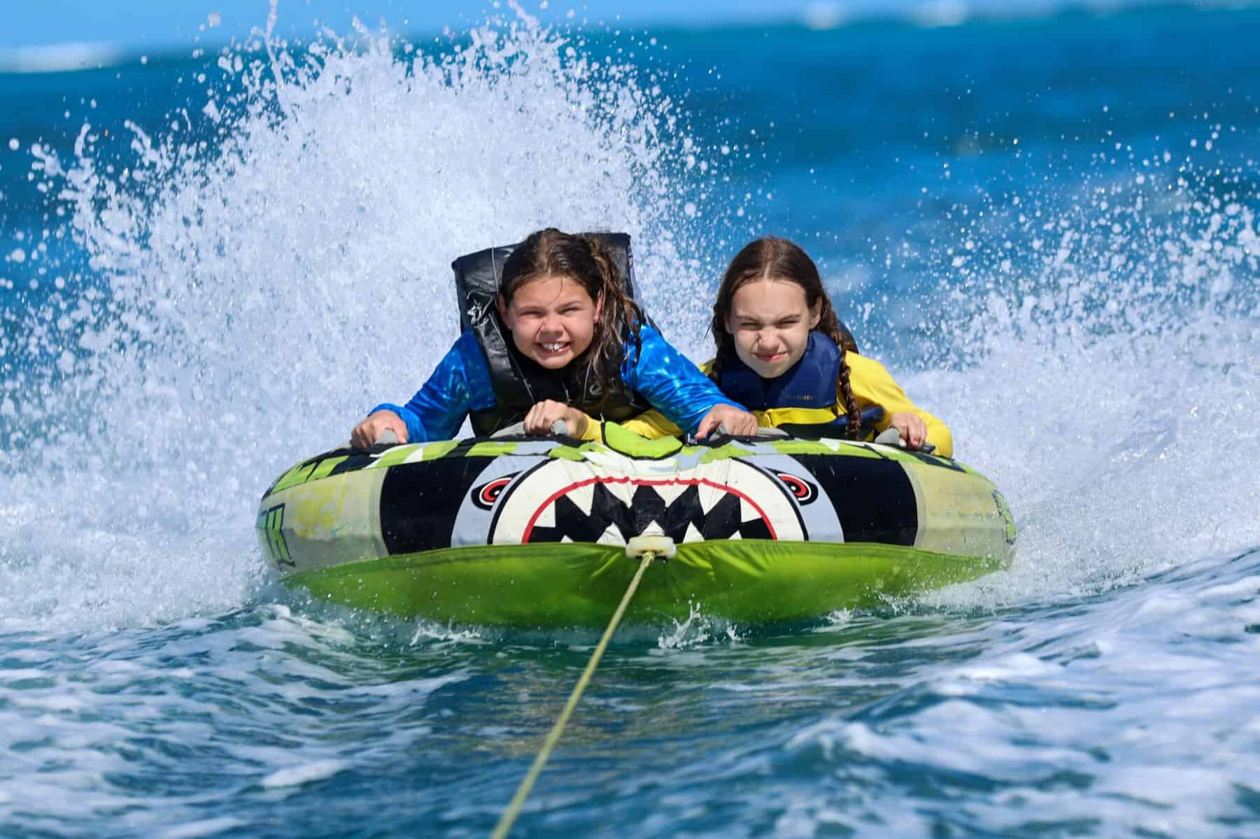 two girls being towed on a tube with water splashing behind them