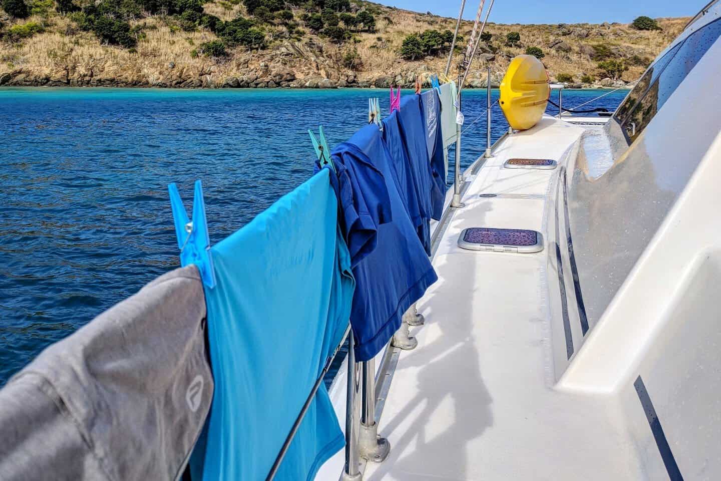 Blue dryfit clothing hung with clothespins on a sailing catamaran in the Caribbean with an island hill in the background