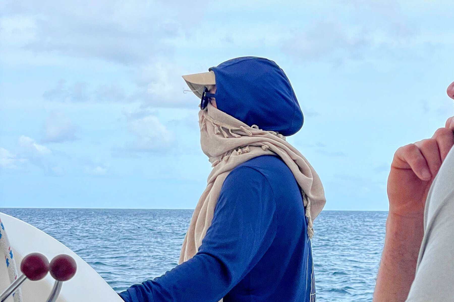 Girl wearing longsleeve dryfit shirt with ballcap and scarf for sun protection on a sailing trip with the ocean in the background
