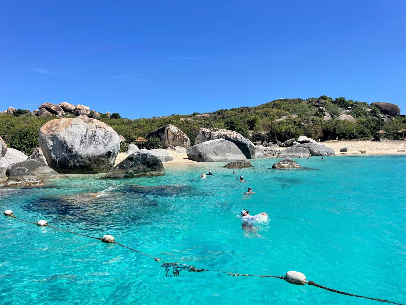 people swimming into The Baths in the British Virgin Islands with the boulders and beach in the background and floating swim-line in the foreground
