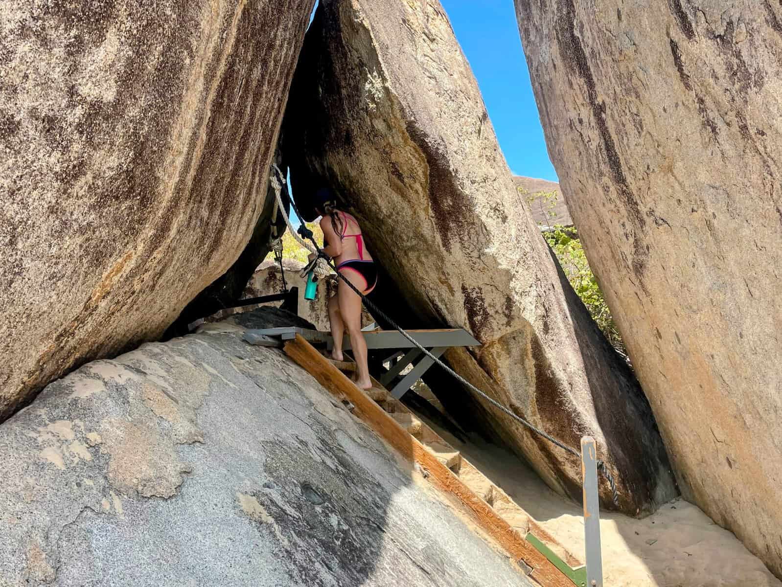 girl in bathing suit climbing ladder into boulders at the Baths British Virgin Islands
