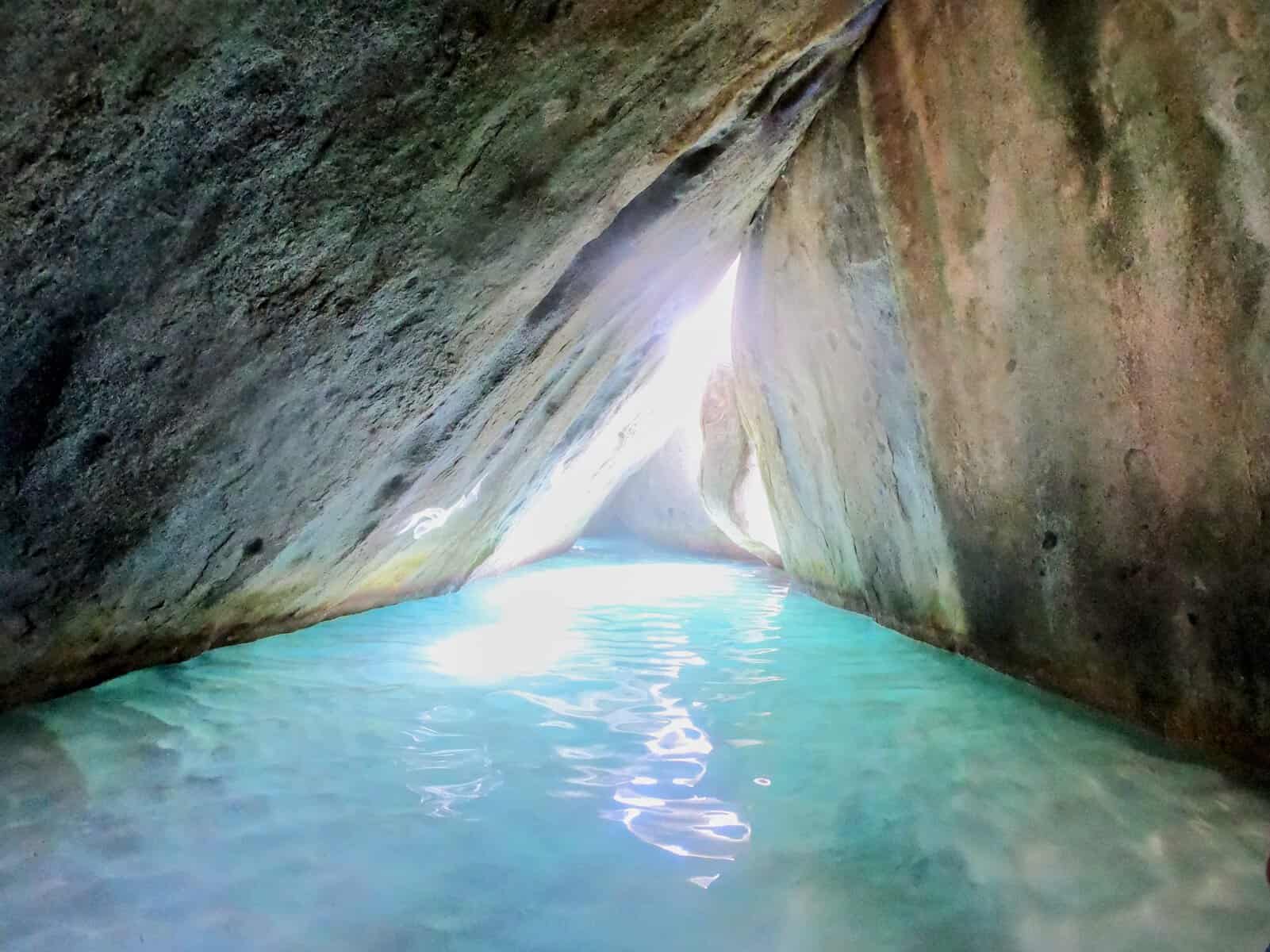 Cathedral room with sun shining through cave-like triangle rock formations in the Baths British Virgin Islands with clear turquoise water