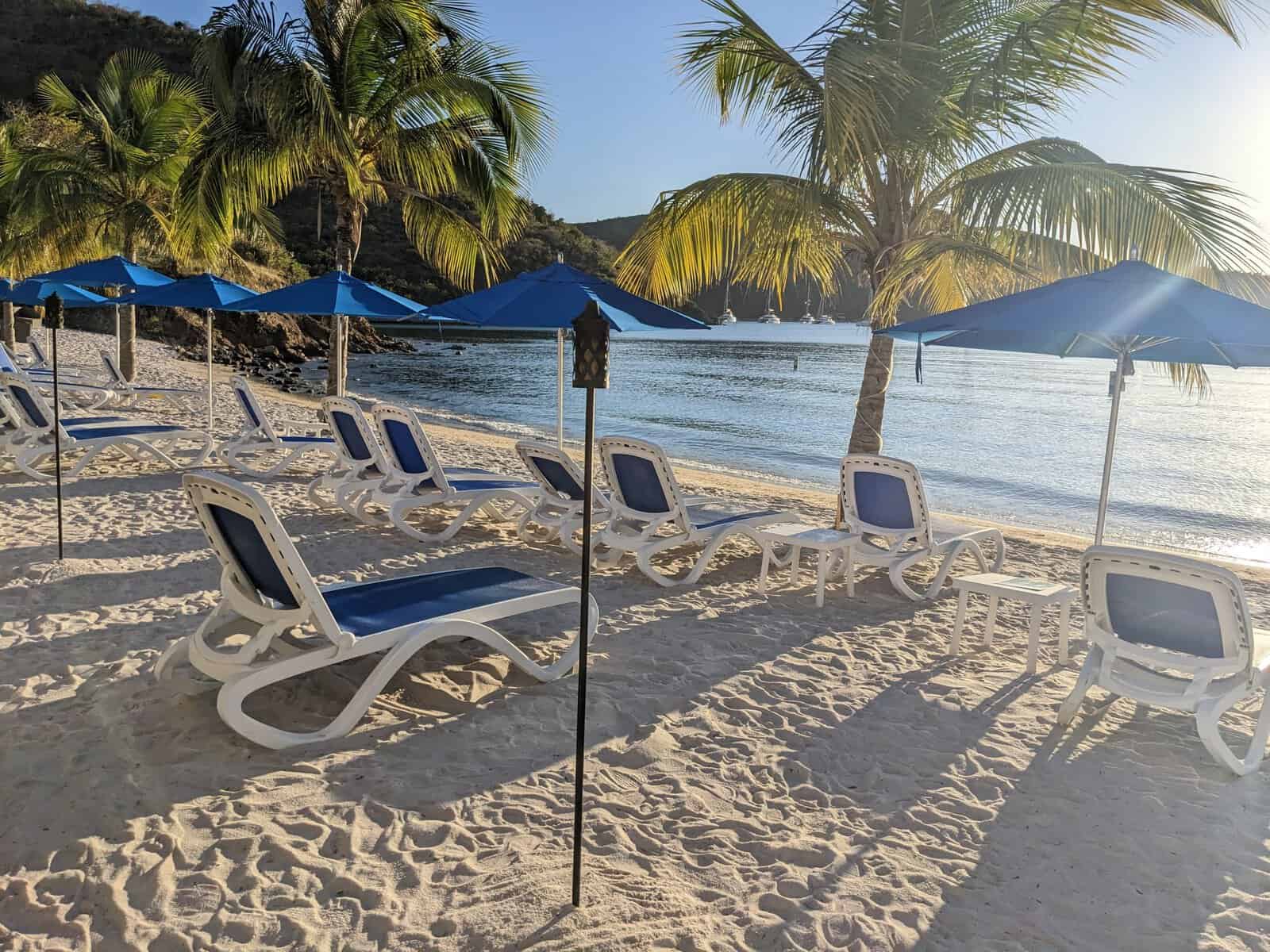 Pirates Bight, Norman Island, British Virgin Islands with white sand, lounge chairs, umbrellas, tiki torches, palm trees, and ocean
