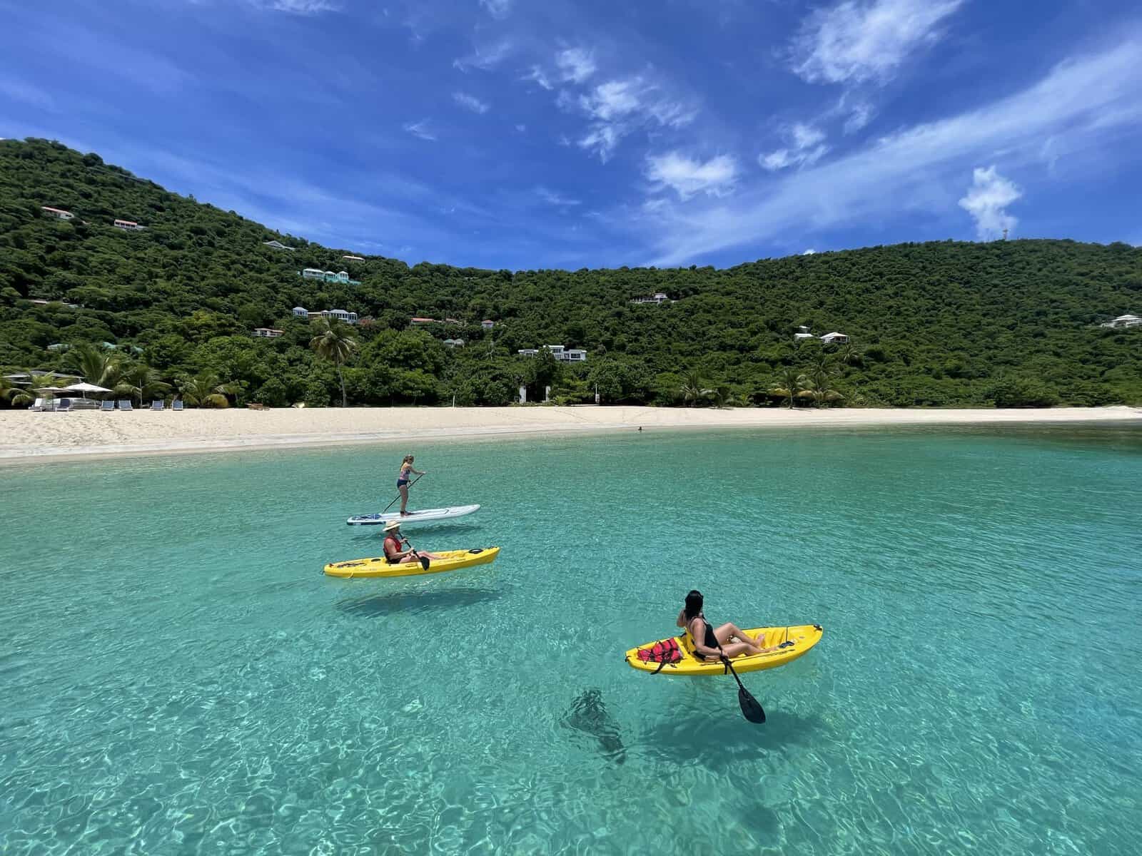 Smuggler's Cove, Tortola, British Virgin Islands. crystal-clear water with people kayaking and SUP with white sand beach and green hillside in background