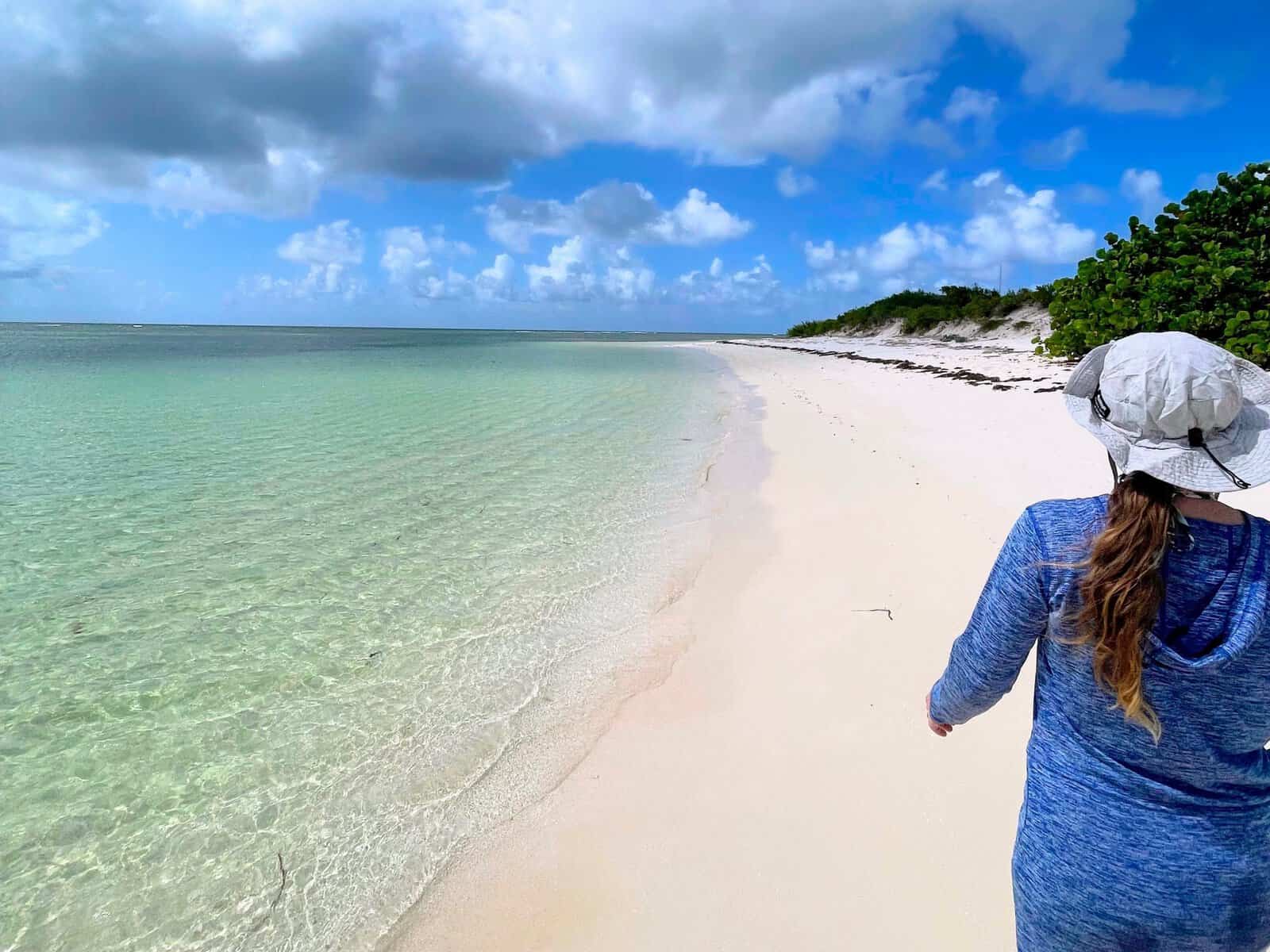 Girl walking along an empty stretch of beach with clear water, white sand and green bushes