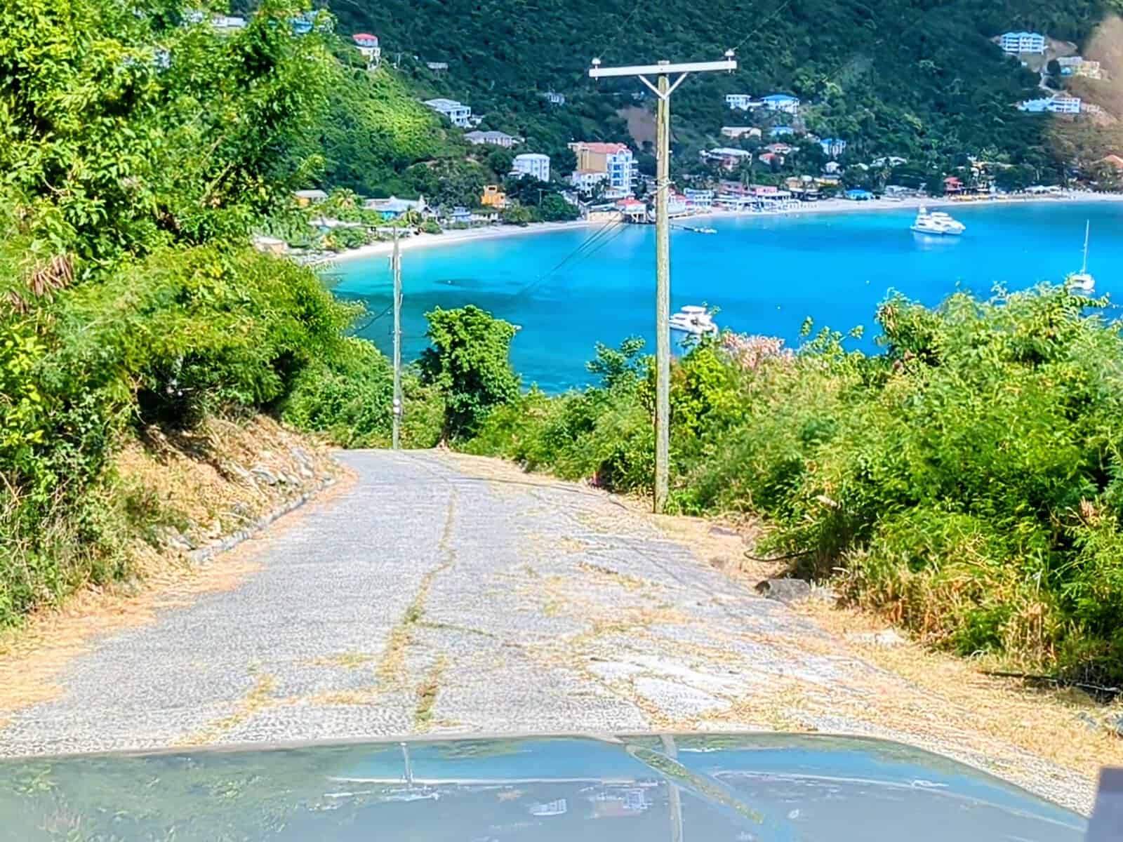 Driving in Tortola - looking out car windshield down steep hill overlooking Cane Garden Bay