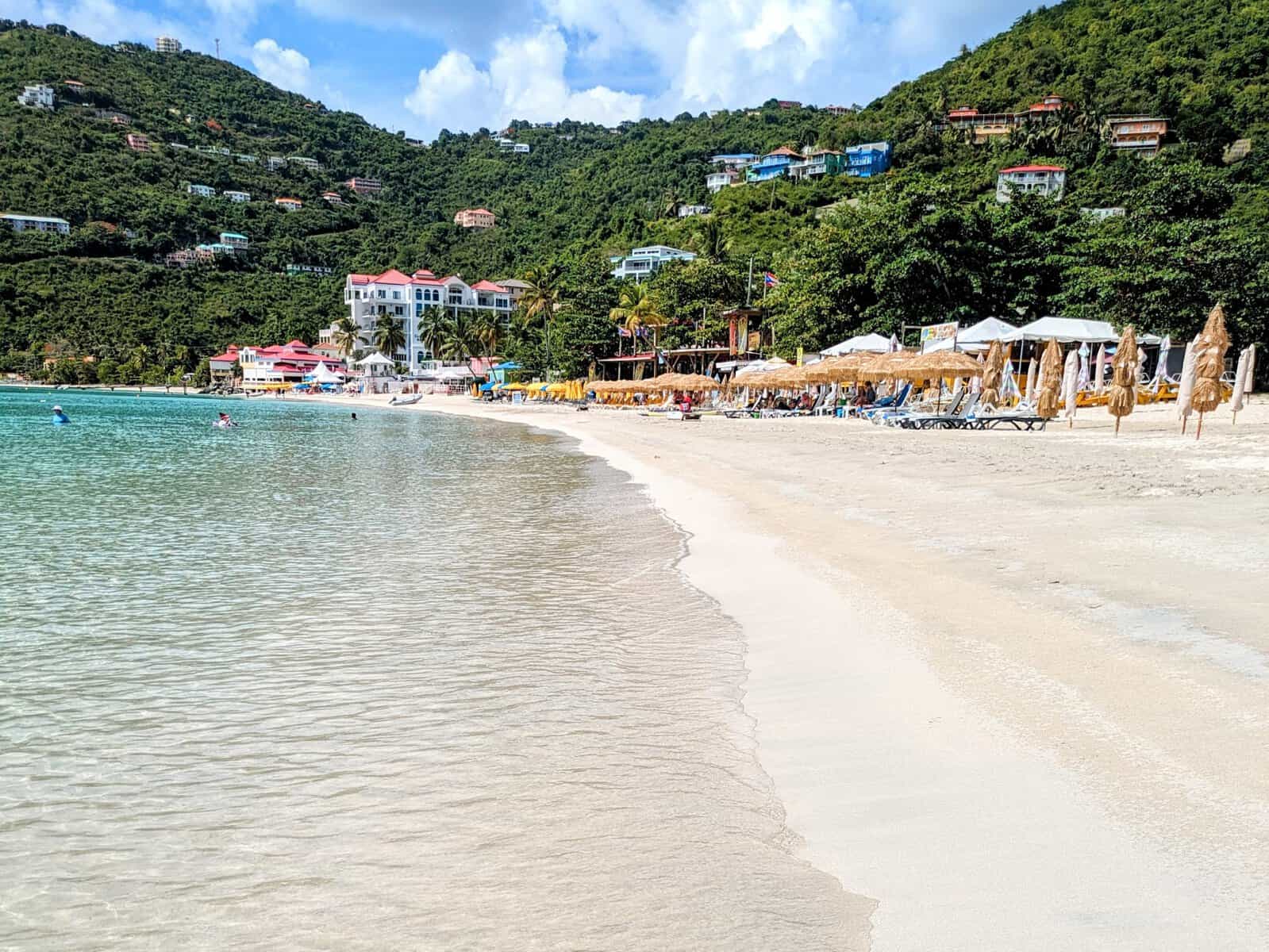Cane Garden Bay, busy beach with thatch umbrellas, clear water and green hills of Tortola 