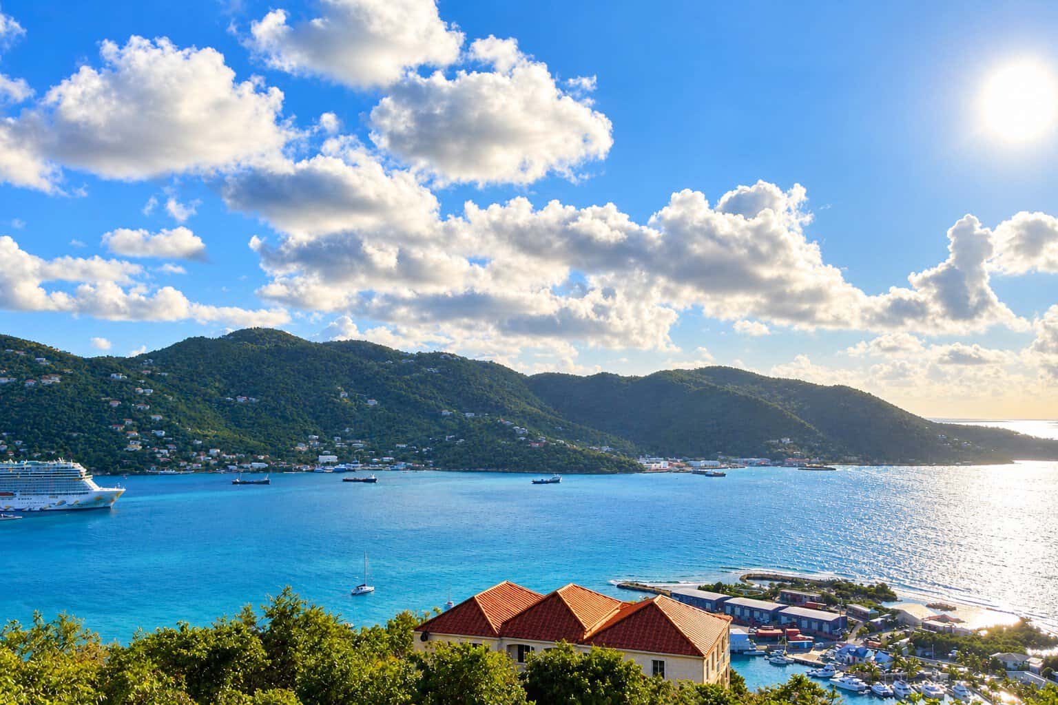Road Town Harbour, Tortola with cruise ship in port, bright blue water, green hills, marina with sailboats, blue sky with sun and white clouds