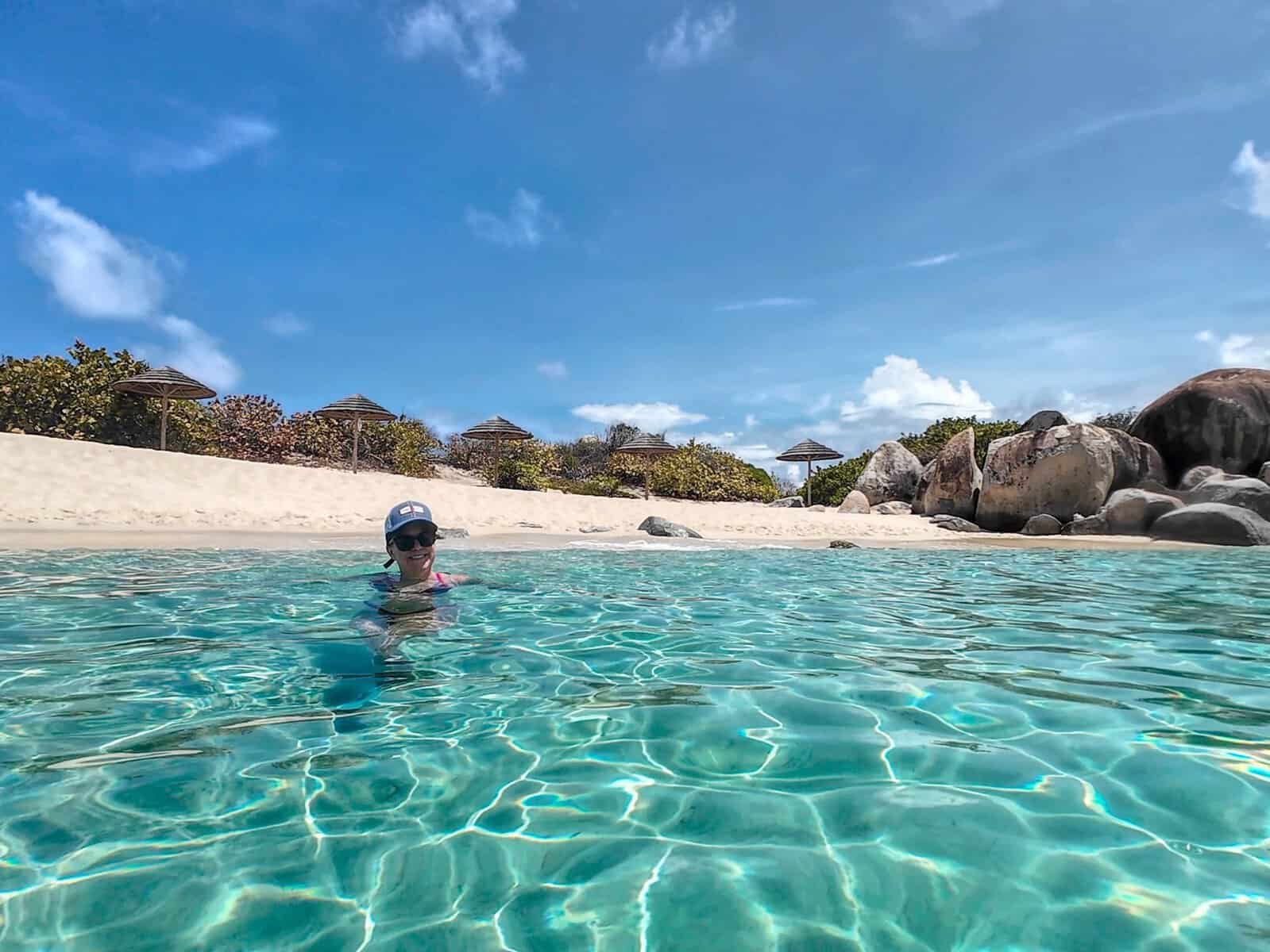 girl in the Caribbean Sea with clear teal water and white-sand beach and boulders