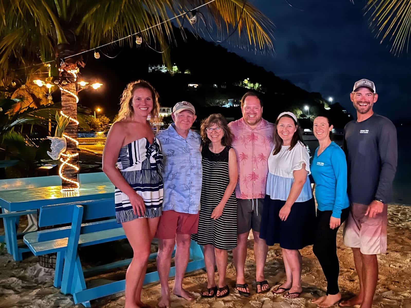 group of adults at Tipsy Shark, Great Harbour, Jost Van Dyke, British Virgin Islands at night under palm tree with twinkle lights and blue picnic table