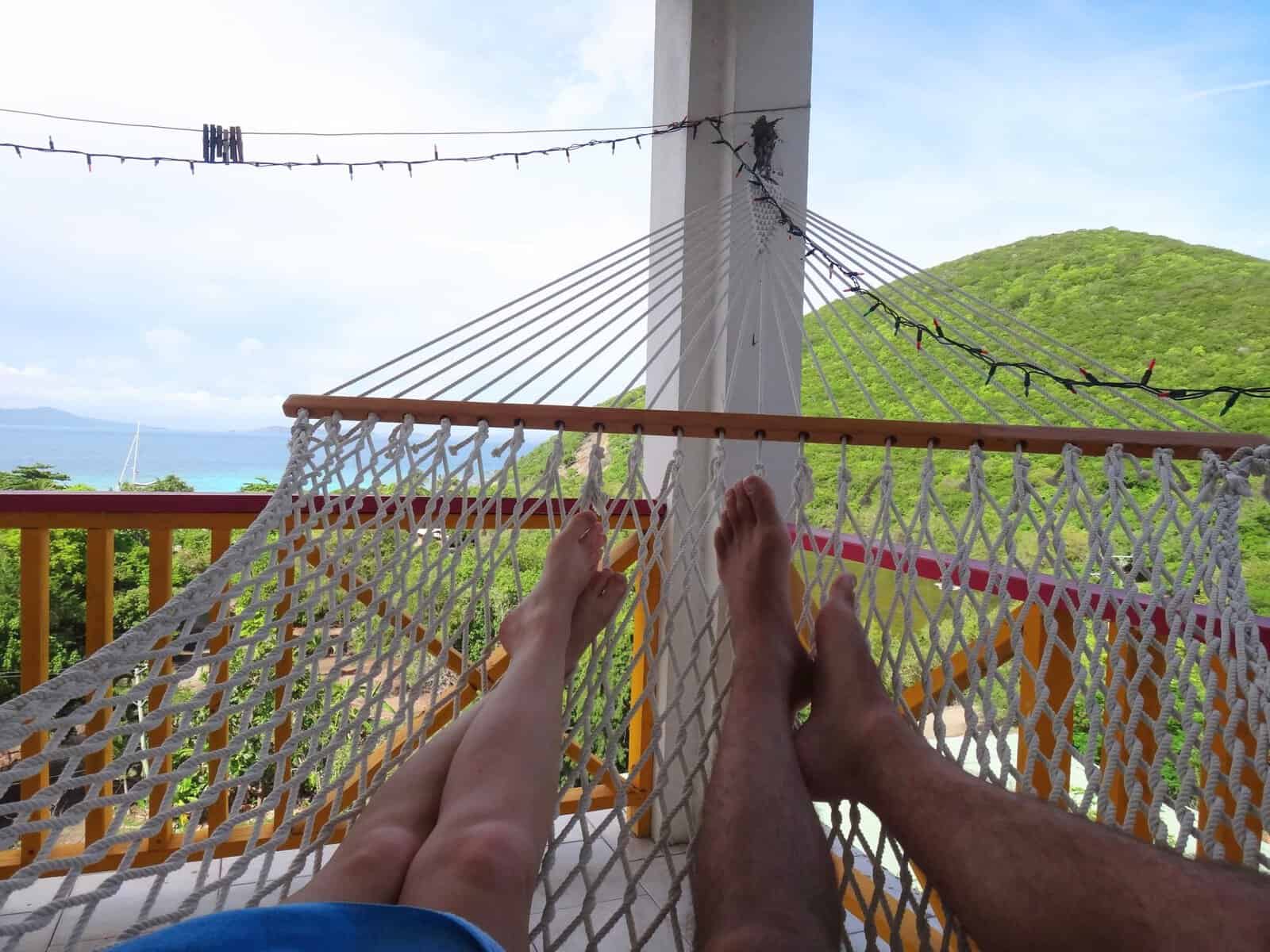 feet swinging in hammock looking over White Bay, Jost Van Dyke, British Virgin Islands with green hills and blue ocean