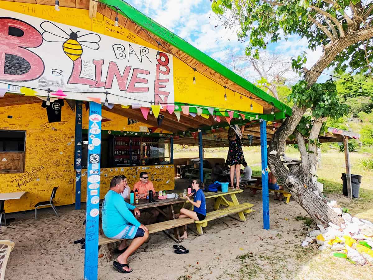 Brightly colored rustic beach bar, B-Line, with people at picnic tables and signing the ceiling. Little Jost Van Dyke, British Virgin Islands